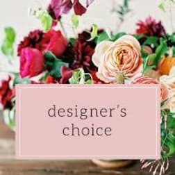 Assorted pink, red, and peach flowers in a vase with a pink designer's choice text panel in front