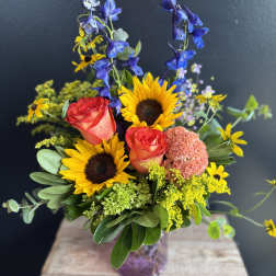 Bouquet with sunflowers, coral roses, and blue delphinium in a glass vase