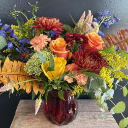 Mixed bouquet of roses, chrysanthemums, and blue flowers in a red glass vase