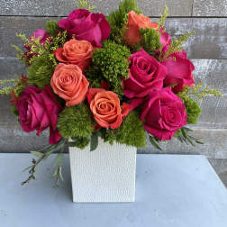 Pink and coral roses arranged in a white square vase