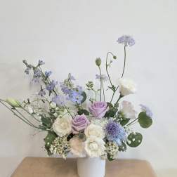 Pastel bouquet of lavender, white, and blue flowers in a white vase