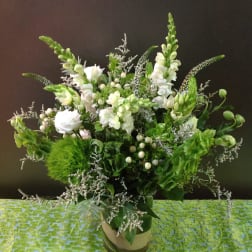 Tall green and white floral arrangement with snapdragons and roses in a clear glass cylinder vase
