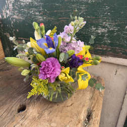 Mixed bouquet with yellow lilies, purple iris, and pink carnations in a glass vase