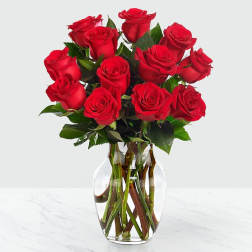 Dozen red roses arranged in a clear glass vase with visible stems.