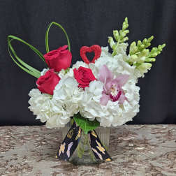Pink roses and white hydrangeas in a glass vase with an orchid accent