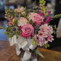 Pink roses and mixed blooms arranged in a glass vase with a white ribbon
