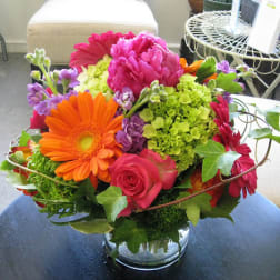 Bright mixed bouquet in a clear glass vase with pink, orange, purple, and green blooms.