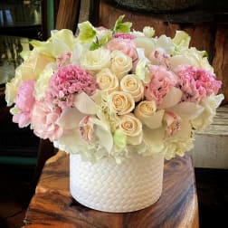 Low round arrangement of white and blush flowers in a white textured cylinder container