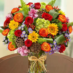 Colorful mixed flower bouquet in a glass vase with a raffia bow
