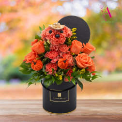 Orange rose and carnation arrangement in a black hatbox with a small straw hat accent