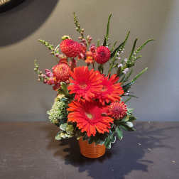 Orange gerbera daisies and pink blooms in a small vase