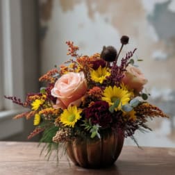 Mixed bouquet of roses and yellow daisies in a copper pumpkin vase