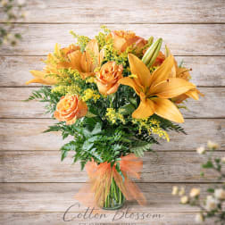 Orange roses and lilies in a glass vase with a sheer ribbon