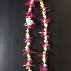 Two purple and white flower leis on a dark surface