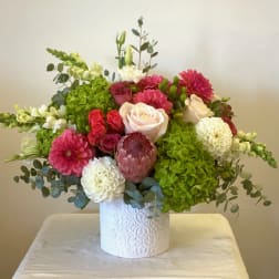 Mixed bouquet with roses, dahlias, hydrangeas, and a protea in a white vase