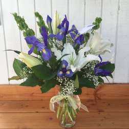 Blue and white iris bouquet in a clear glass vase with a ribbon