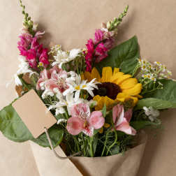 Bouquet of sunflowers, pink alstroemeria, and white daisies in kraft paper