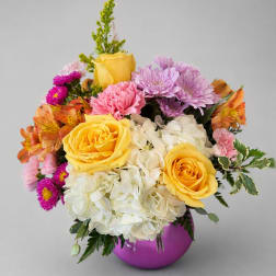 Colorful bouquet of yellow roses, hydrangeas, and mixed blooms in a purple vase