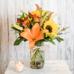 Orange lilies and sunflowers in a glass vase with a candle nearby.