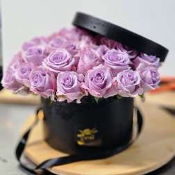 Lavender roses arranged in a black round hat box