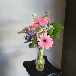 Pink gerbera daisies and purple flowers in a clear glass vase