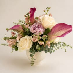 Bouquet of cream roses, pink calla lilies, and carnations in a white vase