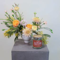 Mixed floral arrangement in a white vase with a jar candle beside it