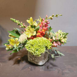 Mixed floral arrangement in a square container with green, yellow, pink, and orange blooms