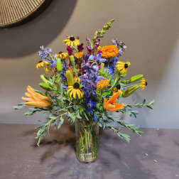Mixed bouquet with orange lilies, yellow daisies, and blue flowers in a glass vase