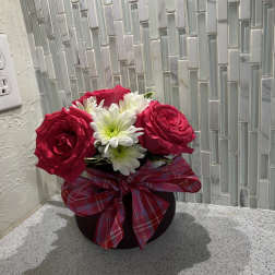 Pink roses and white daisies in a black vase with a plaid bow