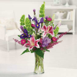 Mixed bouquet of pink lilies, purple flowers, and green spikes in a glass vase