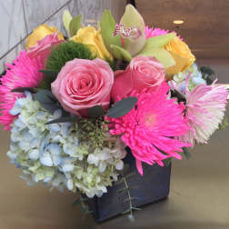Mixed bouquet of pink roses, yellow roses, hydrangea, and bright pink mums in a black vase