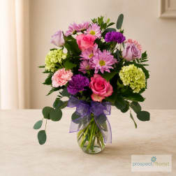 Mixed pink and purple bouquet in a glass vase with a purple ribbon