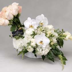 White and blush floral arrangement in a low vase with orchids and roses