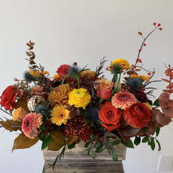 Mixed bouquet of red, yellow, and peach flowers in a wooden container