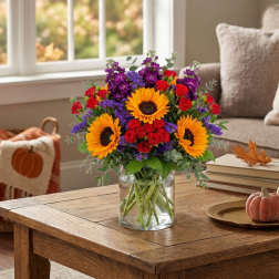 Bouquet of sunflowers, red roses, and purple flowers in a clear glass vase