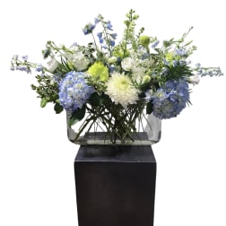 Blue and white floral arrangement in a clear rectangular vase on a black pedestal