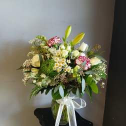 Mixed bouquet of white and yellow flowers in a glass vase with a white ribbon
