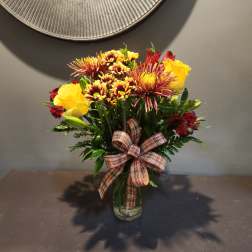 Bouquet of yellow roses and red chrysanthemums in a glass vase with a plaid ribbon
