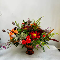 Mixed bouquet in a copper pedestal vase with red, orange, and pink flowers