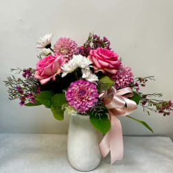 Pink roses and mixed blooms in a white vase with a pink ribbon