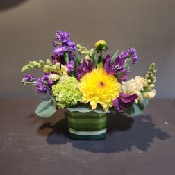 Yellow dahlia bouquet with purple and white flowers in a striped glass vase