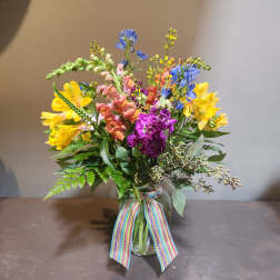 Colorful mixed bouquet in a glass vase with a rainbow ribbon