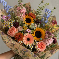 Mixed bouquet with sunflowers, roses, and daisies wrapped in floral paper