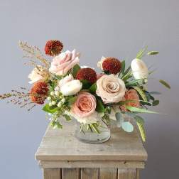 Pink and white roses in a clear glass vase with orange pom-pom flowers