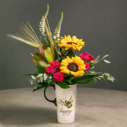 Sunflowers and pink roses arranged in a tall mug with a "happy" design