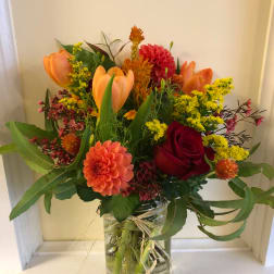 Mixed bouquet of orange tulips, red roses, and a peach dahlia in a glass jar