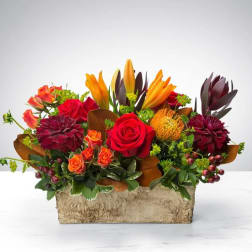 Mixed bouquet with red roses, orange lilies, and burgundy blooms in a rectangular container