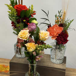 Three floral arrangements in glass vases with roses and carnations