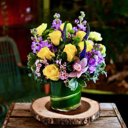Yellow roses and purple flowers arranged in a green glass vase